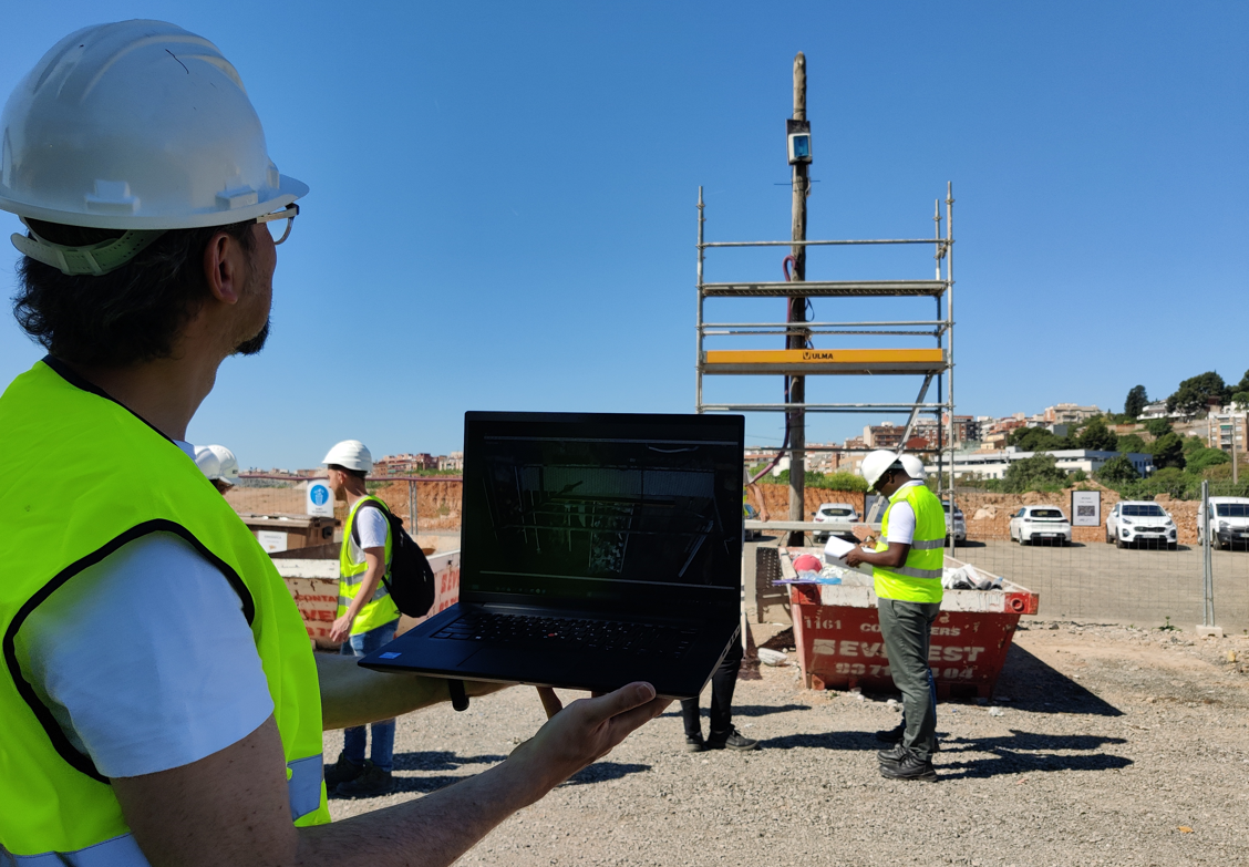 A worker holding a laptop in front of other workers on a construction site